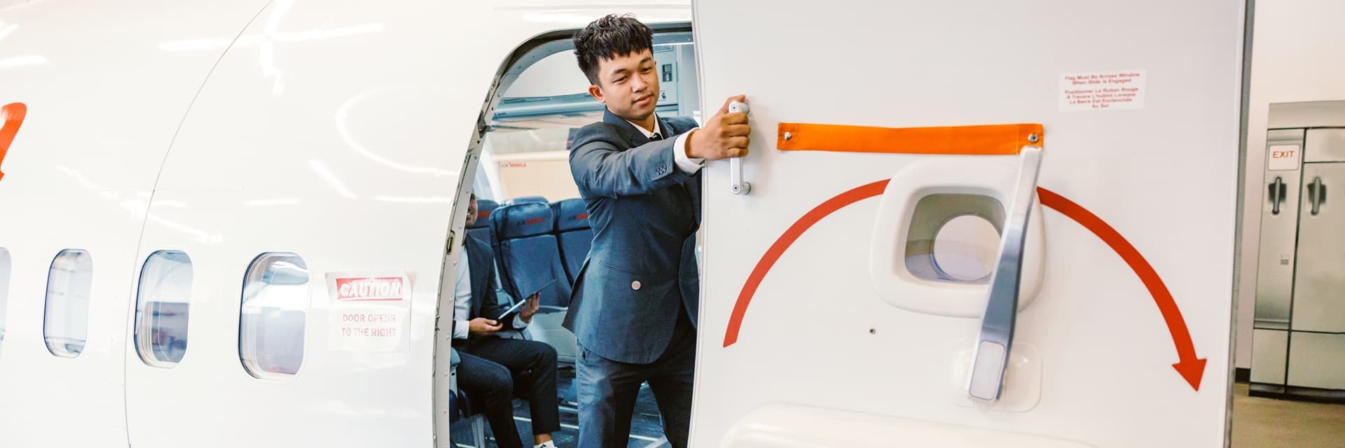 Estudiante de Seneca Polytechnic abriendo la puerta de emergencia en el simulador de cabina del Flights Experiential Hub